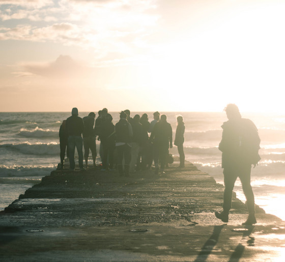 Eine Menschengruppe steht vor dem Meer im Sonnenuntergang auf einem Steg als Titelmotiv für die Psychodynamischen Tage Langeoog 2016.