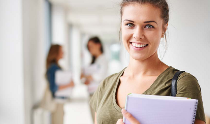 Eine Teilnehmerin blickt auf einem Gang mit weiteren Menschen mit einem Laptop in der Hand lächelnd in die Kamera als Titelmotiv zum Kursprogramm 2027 mit Seminaren, Fort- und Weiterbildungen für das Gesundheitswesen der Albertinen Akademie in Hamburg-Schnelsen.