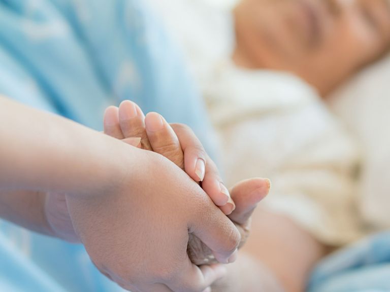 Die Hand einer Pflegefachkraft berührt und hält die Hand einer Patientin in einem Pflegebett als Symbolbild für das Kursangebot für Pflegefachkräfte und therapeutische Berufe der Albertinen Akademie in Hamburg