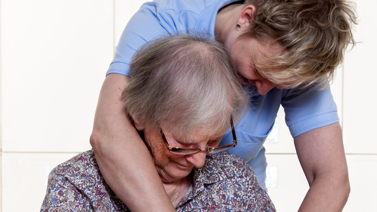 Eine Pflegefachkraft unterstützt eine ältere Frau am Tisch beim Obstschneiden